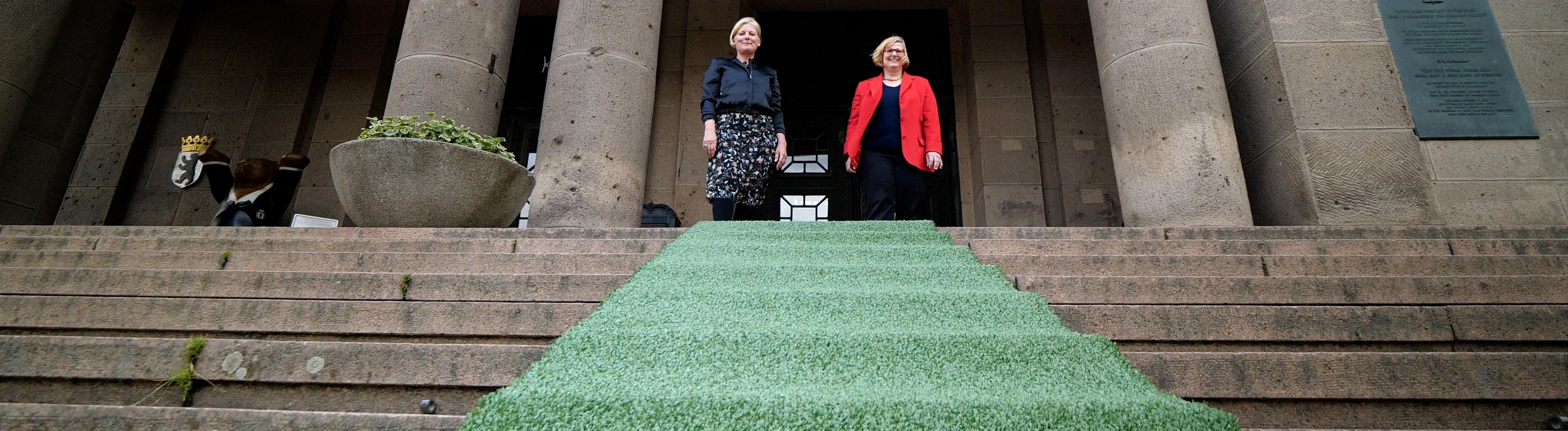 Frau Schöttler und Frau Martina Marijnissen sollen den grünen Teppich vor dem Rathaus aus.