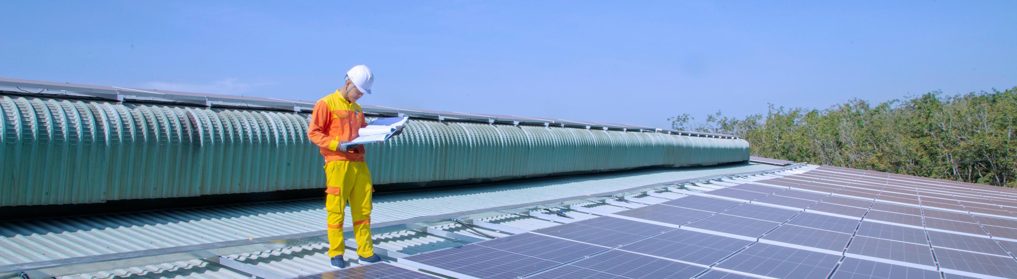 Mann in Arbeitskleidung steht auf großer Photovoltaikfläche, die auf einem Hausdach angebracht ist. 