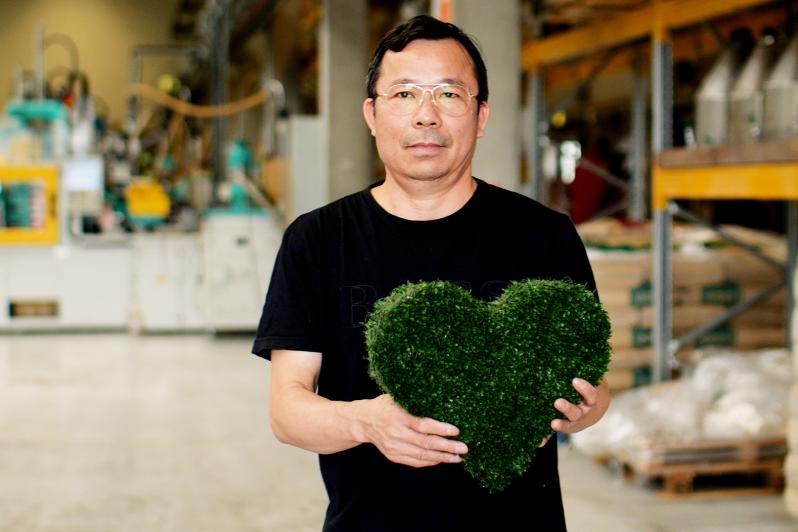 Mann in Produktionshalle mit grünem Herz aus Kunstrasen